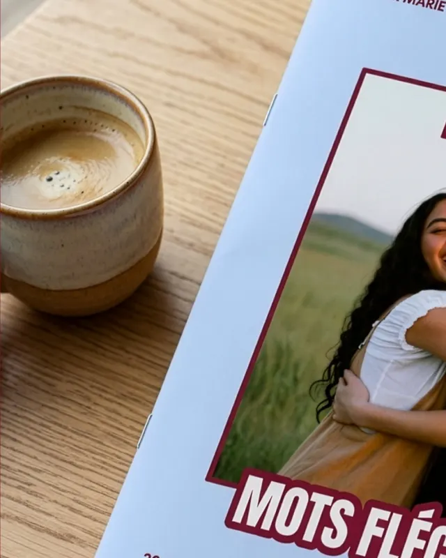 Tasse de café en grès posée sur une table en bois à côté du magazine de mots fléchés